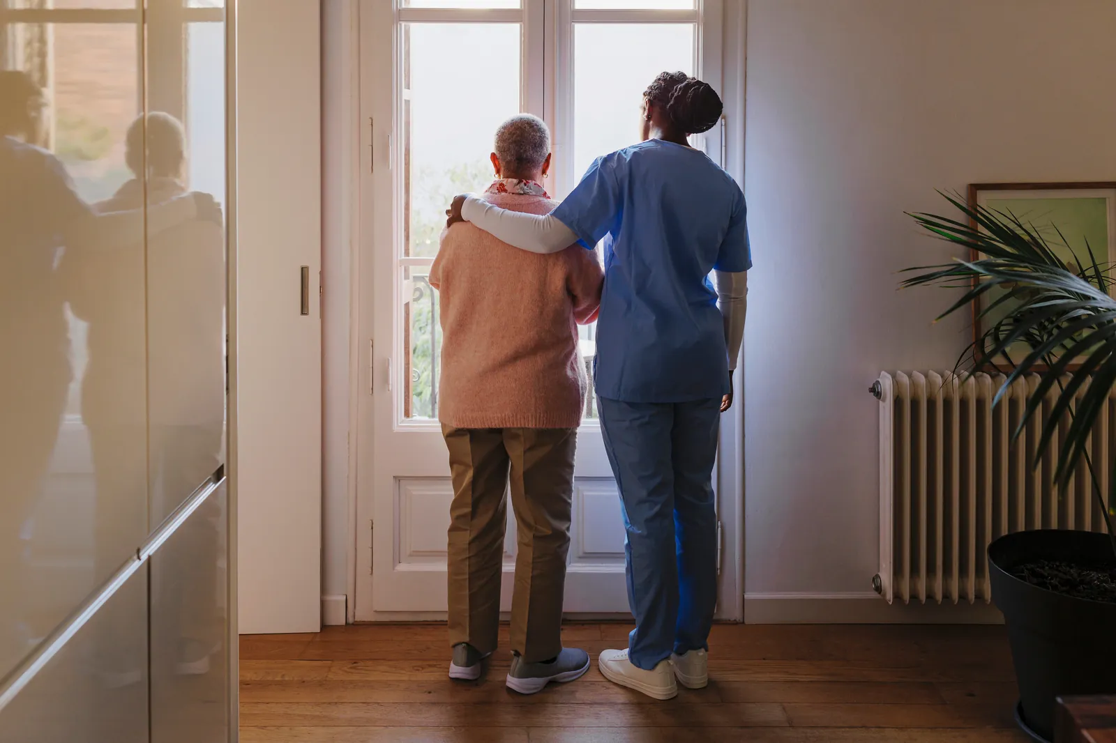 A caregiver and an older man looking out of a window together
