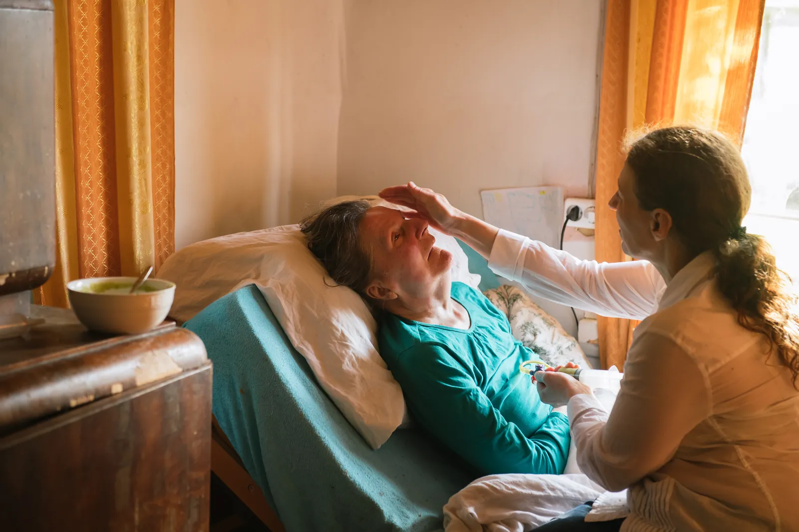 A caregiver at the bedside, gently brushing an older woman’s hair