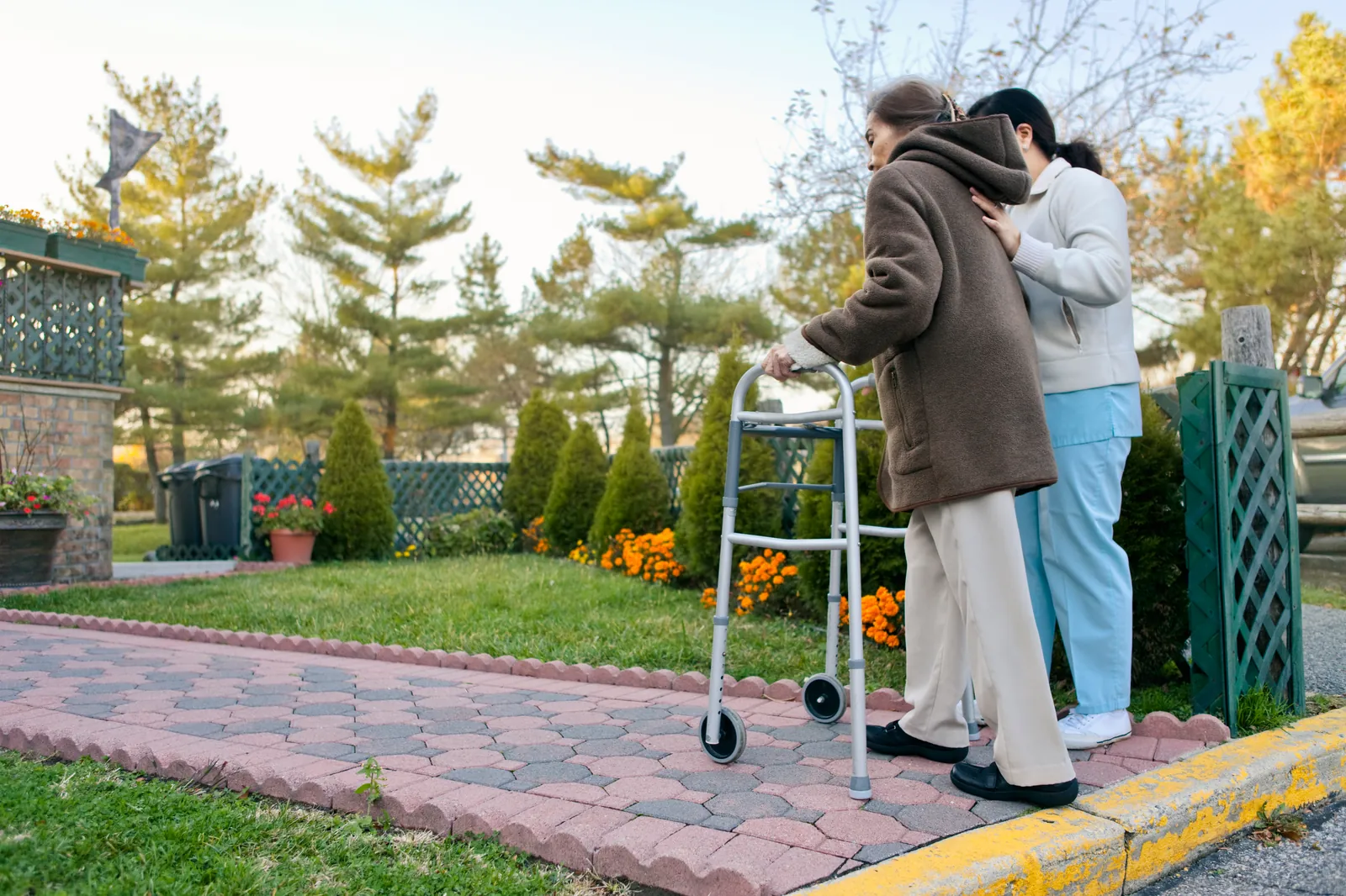 A caregiver walking beside an older woman using a walker in the garden